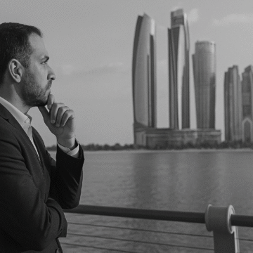 A grayscale image of a man in a suit gazing at the Abu Dhabi skyline, reflecting on the rising Abu Dhabi energy demand.